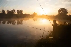 Lonely fisherman angling at foggy lake in the early morning