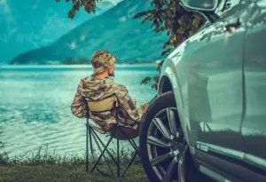 Man sitting down and fishing next to his car