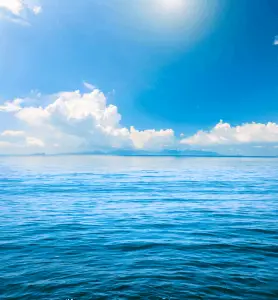 A stunning blue ocean with clouds and sun in the background.