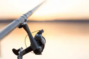 Image of someone fishing at sunset. Close-up fisherman hand with spinning reel