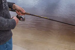 Picture of a young man holding a fishing reel by some water