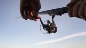 A mans hand holding a spinning fishing reel