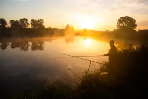 Lonely fisherman angling at foggy lake