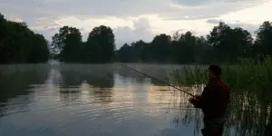 Silhouette of a fisherman standing by the lake and catching the fish