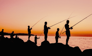 group of people fishing by the shore at sunset