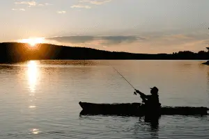 man fishing from a boat in a lake at sunset