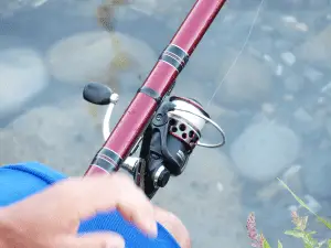 man holding a spinning fishing reel over the lake