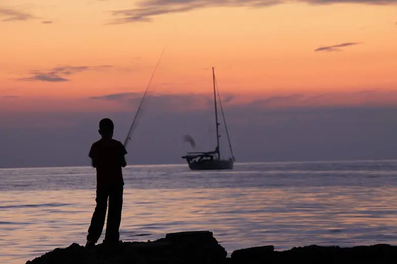 niño pescando al atardecer desde una roca