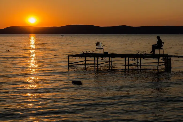 angler fishing from a lake dock at sunset