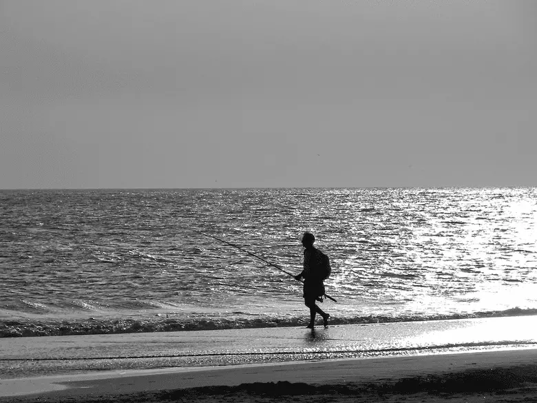 black and white photo of angler fishing near the sea shore