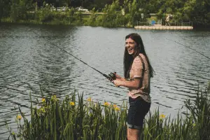 young woman smiling and fishing near the lake