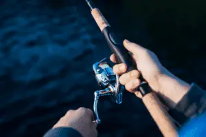 close-up of angler holding a spinning reel over water
