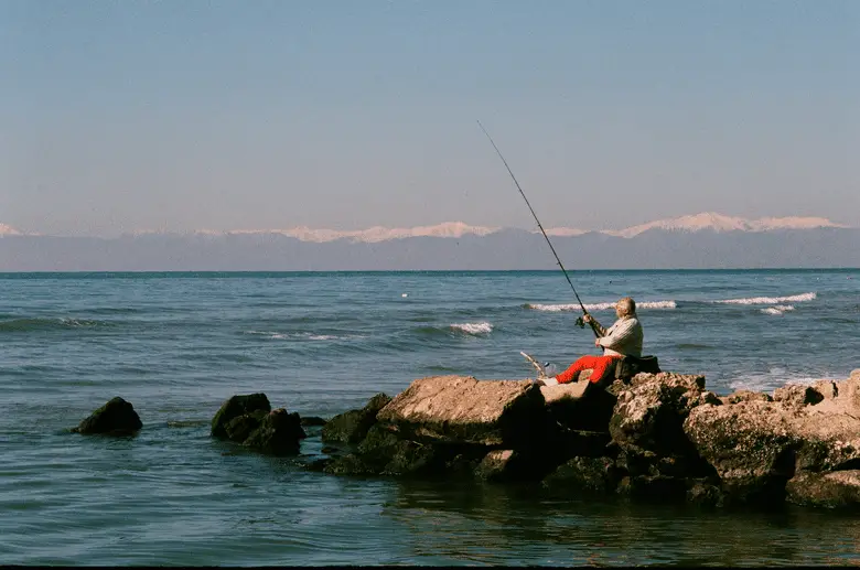 man fishing from a rock near the bay at sunset