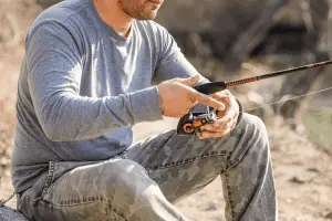 man in gray sweater fishing from the river shore