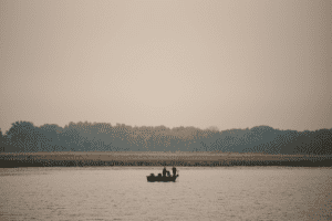 A group of people in a boat on a lake utilizing trolling motors.