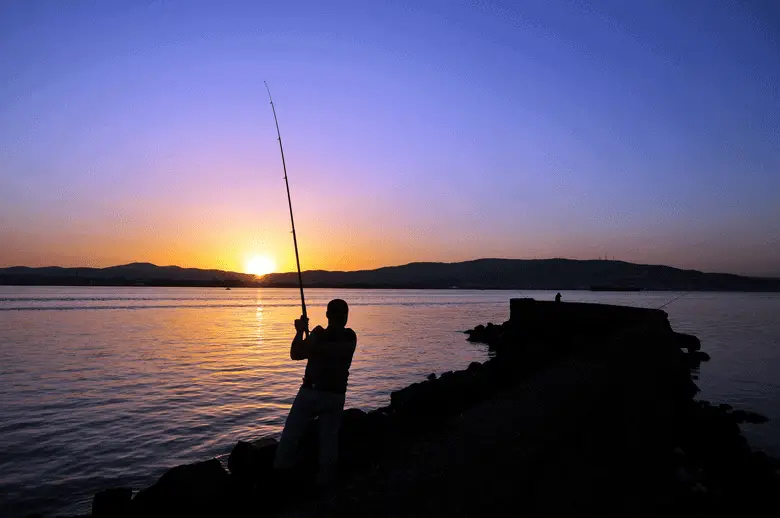 pescador lanzando una caña de pescar al agua al atardecer