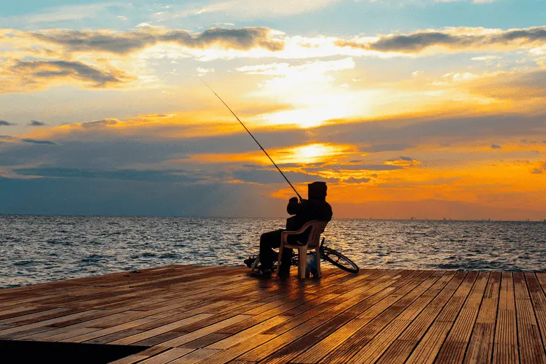 Silhouette of Person Sitting on Chair Holding Fishing Rod Near Body of Water