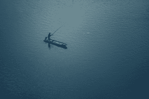 A man is fishing in a small boat on a body of water, using a Daiwa spinning reel.