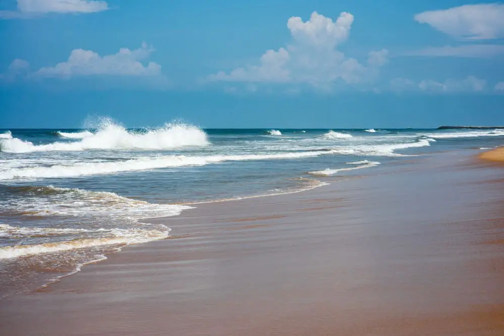 A person is walking on a sandy beach while enjoying the soothing sound of the waves and feeling the soft grains beneath their feet.